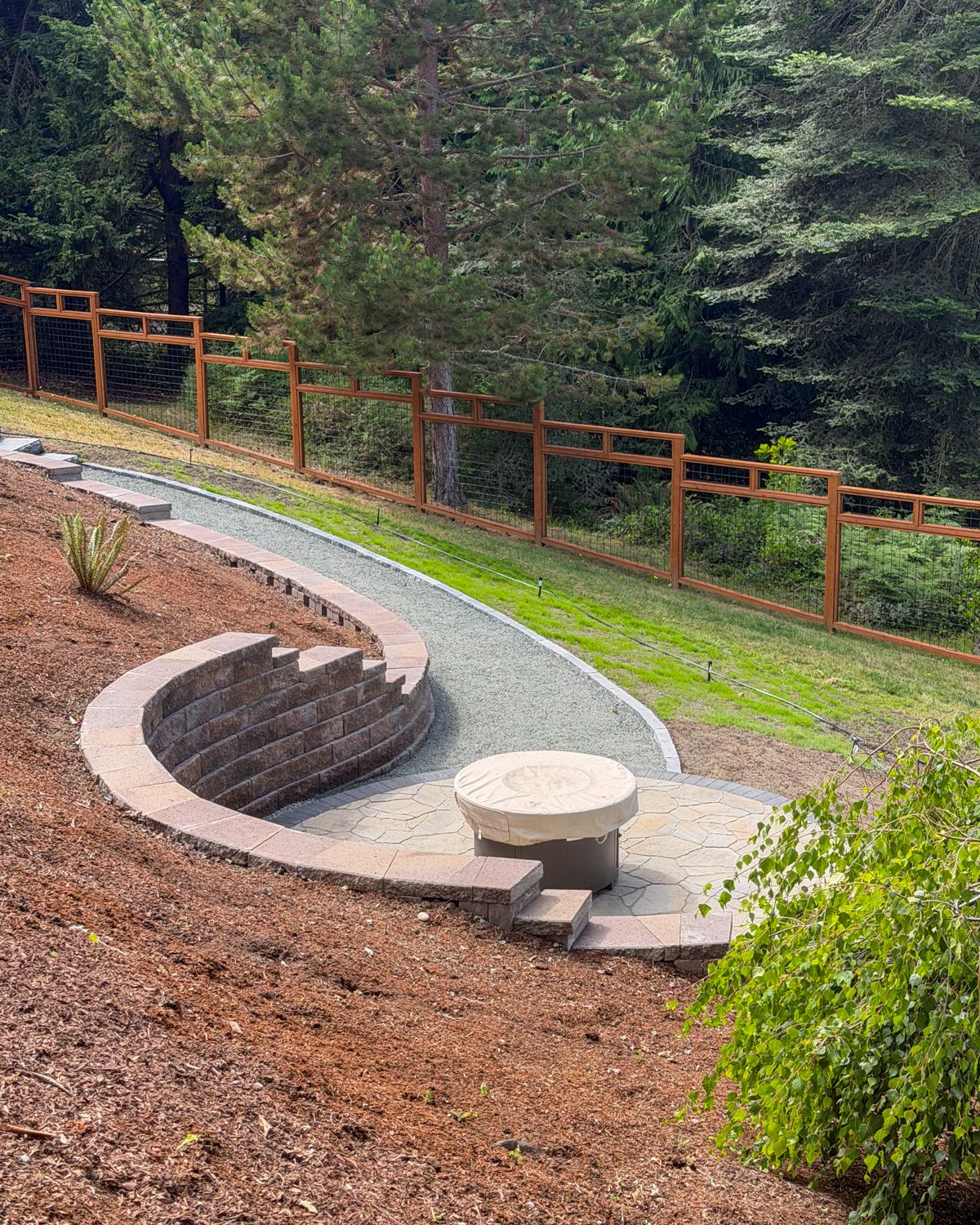 Curved block seat wall around a fire pit patio with a gravel path